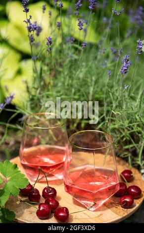 Pique-nique en plein air dans les champs de lavande. Vin de rose dans un verre, cerises sur une planche de bois Banque D'Images