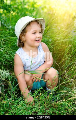 joyeux petit garçon assis dans une herbe verte Banque D'Images