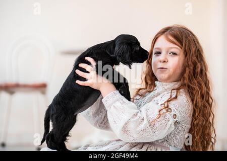 Petite fille roussonne de cheveux rouges jouant avec son nouvel ami, mignon chiot noir Banque D'Images