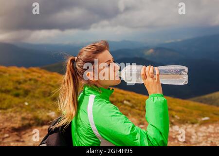 Une jeune femme sportive, randonneur, boit de l'eau tout en grimpant sur la montagne Hoverla dans les Carpates. Voyageur fatigué avec sac à dos de repos. Voyage à l'été Ukrain Banque D'Images