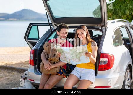 Couple souriant qui vérifie la carte tout en étant assis dans le coffre de la voiture Banque D'Images