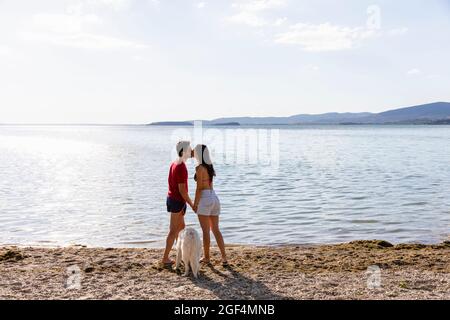 Couple s'embrassant en se tenant près d'un animal de compagnie au bord du lac Banque D'Images