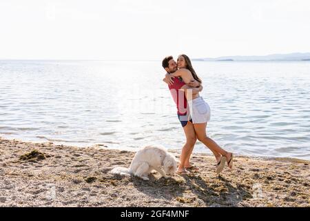 Petit ami transportant tout en embrassant petite amie par chien au bord du lac Banque D'Images