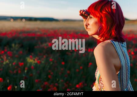 Femme à tête rouge protégeant les yeux tout en regardant loin pendant le coucher du soleil Banque D'Images