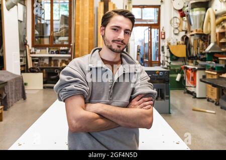 Jeune artisan masculin avec armes croisées à l'atelier Banque D'Images