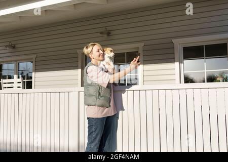Femme prenant le selfie à travers le smartphone avec le chien près de la main courante à l'extérieur de la maison Banque D'Images