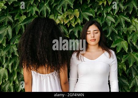 Femme avec les yeux fermés debout près d'une amie femelle face aux plantes Banque D'Images