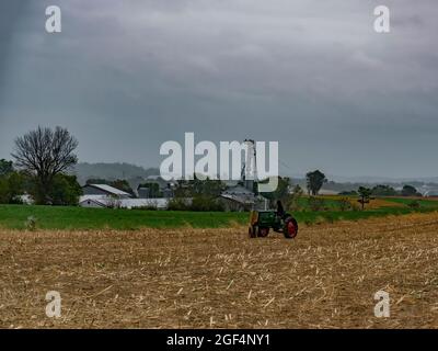 Old Antique restauré suivi de ferme avec une personne sur lui assis dans un champ récolté dans la pluie Banque D'Images