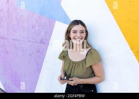 Femme souriante tenant un smartphone devant un mur coloré Banque D'Images