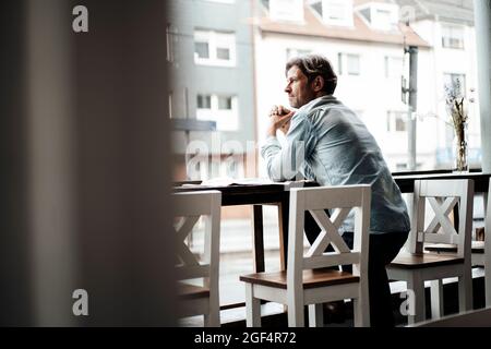 Homme mûr avec les mains claspétées s'appuyant sur une table debout dans un café Banque D'Images