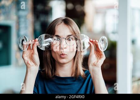 Jeune femme regardant à travers des lunettes de vin dans le café Banque D'Images