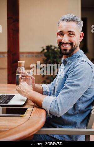 Homme souriant indépendant ayant de l'eau au bureau dans l'arrière-cour Banque D'Images