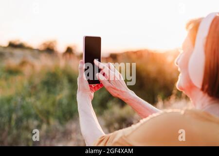 Femme âgée utilisant un téléphone mobile pendant la randonnée au coucher du soleil Banque D'Images