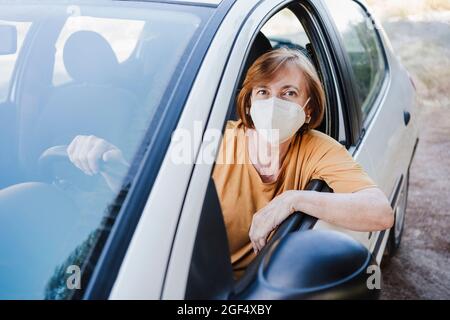Femme âgée avec masque de protection assise en voiture pendant COVID-19 Banque D'Images
