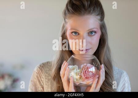 Belle femme blonde tenant des roses parfumées dans un bol en verre Banque D'Images