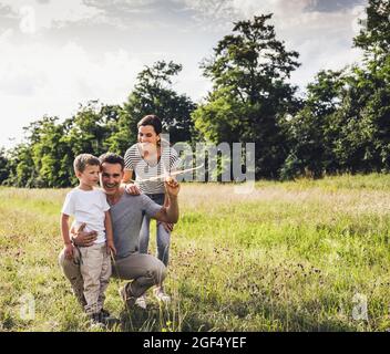 Père tenant un jouet d'avion tout en croupirant par son fils et la femme sur l'herbe Banque D'Images