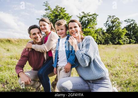 Les parents souriants s'accroupient avec les enfants par beau temps Banque D'Images