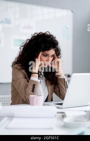 Femme d'affaires tentée avec la tête dans les mains assis au bureau Banque D'Images