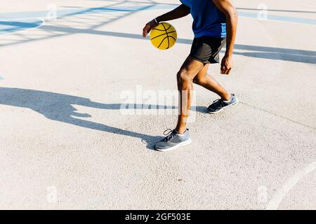 Un jeune homme dribbling basket-ball sur le terrain de sport pendant la journée ensoleillée Banque D'Images