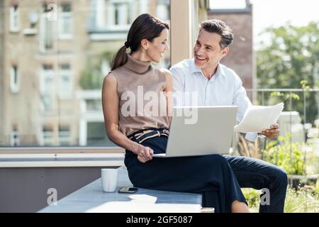 Femme d'affaires en discussion avec un collègue assis sur un mur de soutènement Banque D'Images