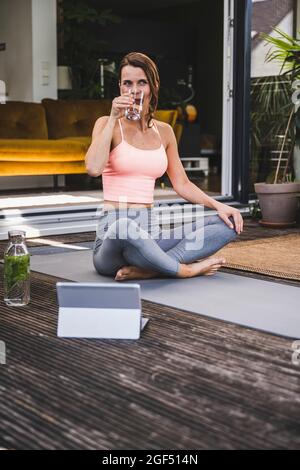 Femme buvant de l'eau de détox tout en étant assise à pieds croisés sur la terrasse Banque D'Images