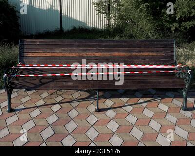 Banc peint en bois recouvert de ruban de protection sur les dalles de pavage par temps ensoleillé Banque D'Images