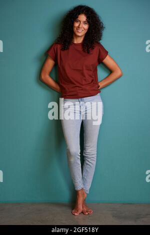 Femme souriante debout avec les mains derrière le dos au mur Banque D'Images