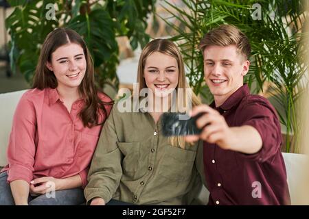Un homme heureux qui prend son selfie sur un smartphone avec des collègues féminins au bureau Banque D'Images