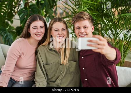 Homme d'affaires souriant prenant le selfie par téléphone portable avec des collègues féminins au bureau Banque D'Images