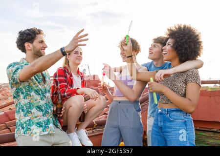 Des amis gais et multiethniques jouent avec des bulles sur le toit Banque D'Images