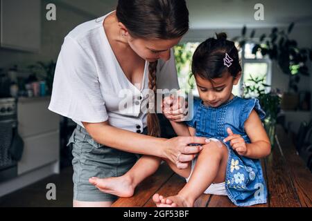 Mère tenant la main tout en mettant le bandage sur le genou de la fille à la maison Banque D'Images