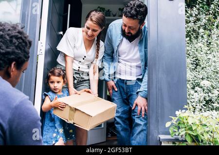 Parents souriants regardant la fille qui reçoit le colis de la personne de livraison Banque D'Images