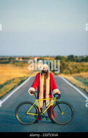 Homme en costume du Père Noël debout avec vélo sur la route Banque D'Images