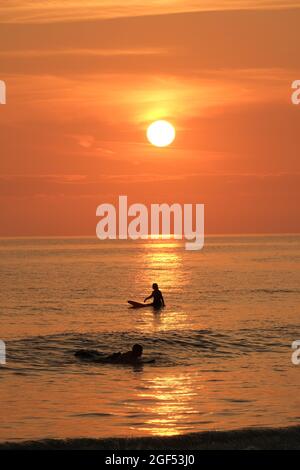 Gower, Swansea, Royaume-Uni. 23 août 2021. Météo au Royaume-Uni : les surfeurs attendent une vague sous le soleil couchant une belle soirée avec quelques nuages fins et un soleil brumeux à la plage de Llangennith sur la péninsule de Gower. Les perspectives pour la semaine à venir sont pour le même beau temps qui devrait être chaud parfois mais pas chaud. Crédit : Gareth Llewelyn/Alay Banque D'Images