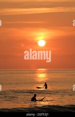 Gower, Swansea, Royaume-Uni. 23 août 2021. Météo au Royaume-Uni : les surfeurs attendent une vague sous le soleil couchant une belle soirée avec quelques nuages fins et un soleil brumeux à la plage de Llangennith sur la péninsule de Gower. Les perspectives pour la semaine à venir sont pour le même beau temps qui devrait être chaud parfois mais pas chaud. Crédit : Gareth Llewelyn/Alay Banque D'Images