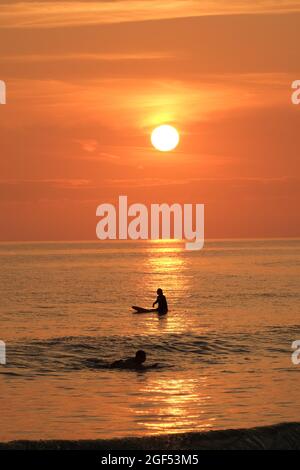 Gower, Swansea, Royaume-Uni. 23 août 2021. Météo au Royaume-Uni : les surfeurs attendent une vague sous le soleil couchant une belle soirée avec quelques nuages fins et un soleil brumeux à la plage de Llangennith sur la péninsule de Gower. Les perspectives pour la semaine à venir sont pour le même beau temps qui devrait être chaud parfois mais pas chaud. Crédit : Gareth Llewelyn/Alay Banque D'Images