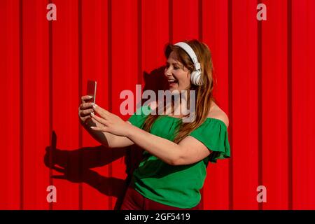 Une femme joyeuse qui prend son selfie à travers un smartphone tout en écoutant de la musique Banque D'Images