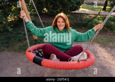 Jeune femme souriante assise sur une balançoire dans l'aire de jeux Banque D'Images