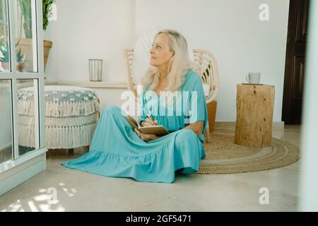 Femme attentionnés assise avec un livre sur la moquette à la maison Banque D'Images