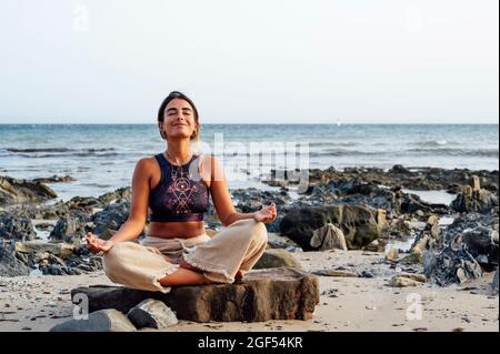 Femme souriante méditant sur le rocher à la plage Banque D'Images