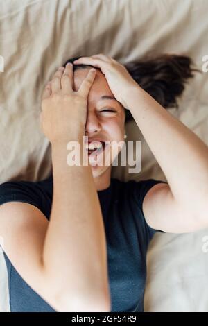 Bonne fille couvrant le visage tout en étant couché sur le lit à la maison Banque D'Images