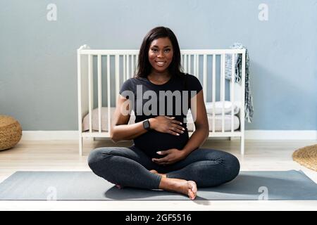 Bonne jeune femme enceinte assise à pattes croisées sur un tapis d'exercice à la maison Banque D'Images