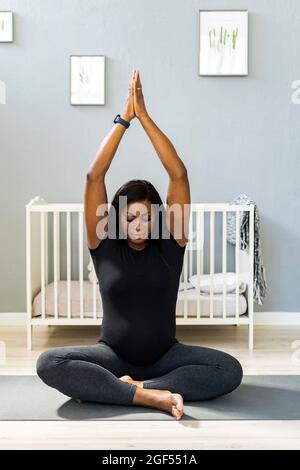 Jeune femme enceinte aux bras élevés pratiquant le yoga à la maison Banque D'Images