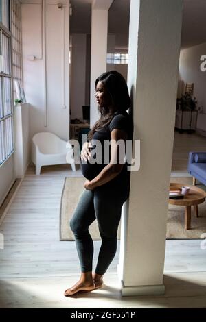 Femme enceinte se penchant contre la colonne à la maison Banque D'Images