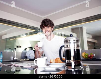Jeune homme souriant prenant un café dans la cuisine Banque D'Images