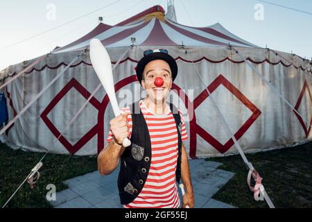 Clown masculin souriant tenant la broche de jonglage tout en se tenant devant la tente de cirque Banque D'Images