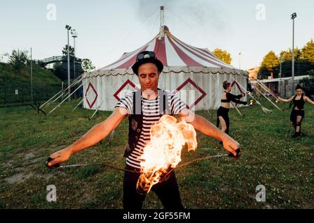 Danseuse de feu de sexe masculin tenant un équipement de feu tout en pratiquant devant une tente de cirque Banque D'Images