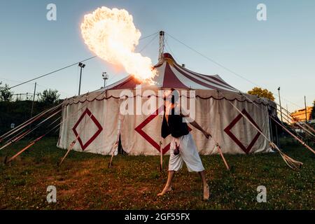 Un mâle acrobat souffle le feu en se tenant devant la tente de cirque Banque D'Images