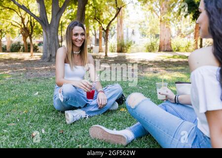 Des amies qui se servent de boissons tout en étant assises dans le parc Banque D'Images