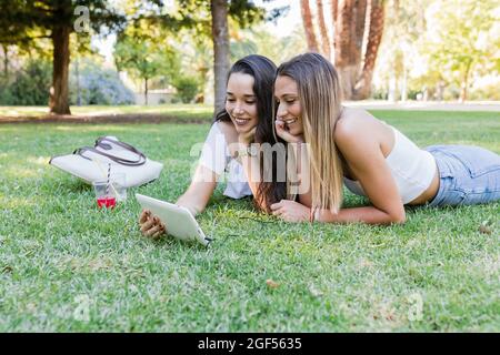 Jeunes amies avec des amis qui utilisent une tablette numérique tout en étant au parc Banque D'Images